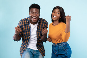 Portrait of excited young black couple shaking clenched fists