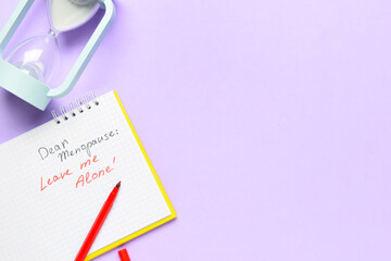 Notebook with text DEAR MENOPAUSE LEAVE ME ALONE and hourglass on lilac background