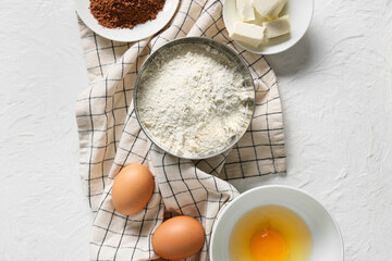 Bowl with flour and ingredients for preparing chocolate brownie on white background