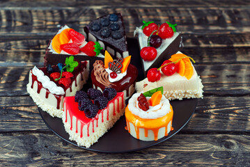 Set of different cakes on a black background. Pieces of cakes with chocolate and fruit icing. Sweets on a brown wooden table. - obrazy, fototapety, plakaty