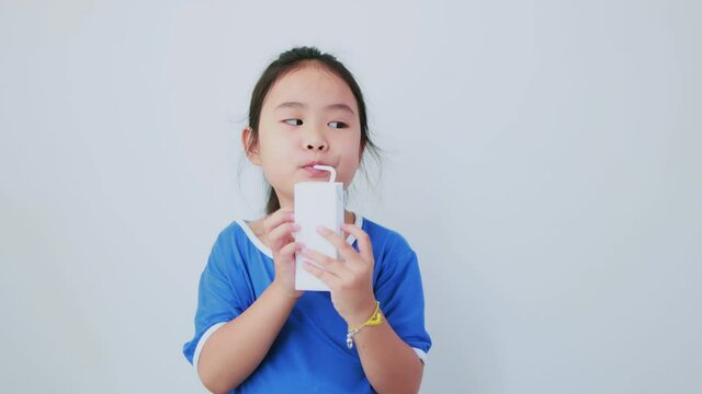 Asian girl trying to drink from an unlabelled white milk carton with a funny face when she tasted it. Half body camera angle on white background.