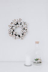 Cotton flower wreath hanging on white wall. Living room modern minimalistic interior decoration.