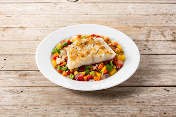 Grilled cod with vegetables in plate on wooden table	

