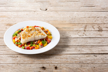 Grilled cod with vegetables in plate on wooden table. Copy space
