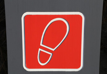 A close up view of a red and white sign with footprint symbol indicating the way to a visitor centre in Wales, UK.