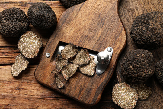 Shaver with whole and sliced black truffles on wooden table, flat lay