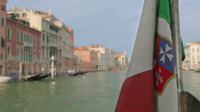 Italian maritime flag waving during boat ride on Grand Canal, Venice, Italy, at day. Medieval buildings in background, selective focus