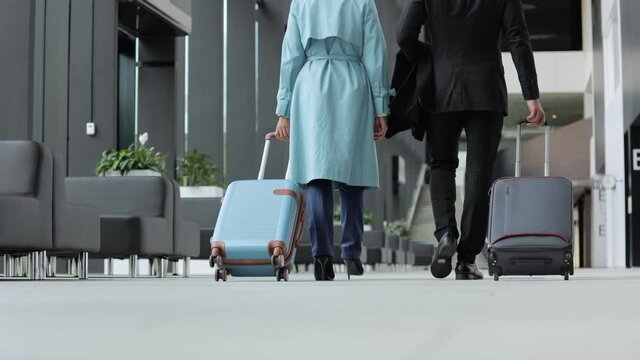 Back view of man, woman with suitcases in hands walking around airport interior spbi. Young businesswoman, businessman hold luggage and talk with smiles, walk in lounge area and expect departure or