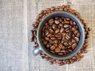 a dark gray mug filled with roasted whole coffee beans stands on a wooden background with coffee beans. top view. energy