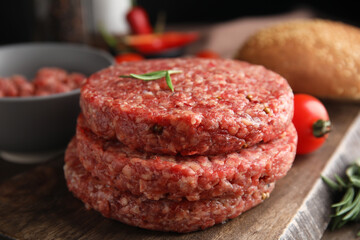 Raw hamburger patties with rosemary on wooden board, closeup