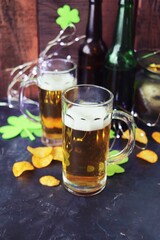 Patrick's Day, foamy beer in glass mugs and a bottle, crackers, gold coins and a green shamrock on a wooden background, party, congratulation, postcard