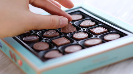 Woman take one chocolate from a box of different candies. Close-up. heart shaped candy, valentine's day