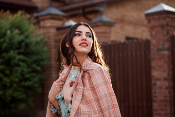 Portrait of romantic woman dressed in a checkered pink jacket in front of the red brick building, sunset.