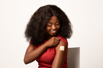 Immunization Concept. Vaccinated Black Female Looking At Her Arm With Adhesive Bandage