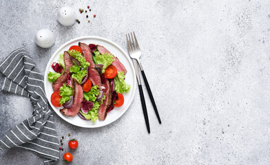 Salad with beef, lettuce and tomatoes on a concrete background.