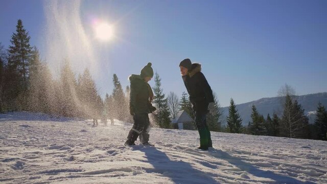 Mother and son playing with snow on the winter mountain. Happy family plays together outside. Winter family activities.