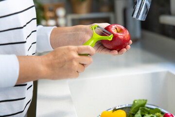 Young woman peeling an apple with peeler in kitchen by faucet.