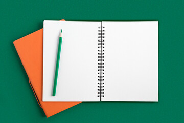 Notebook with pencil. Open notebook on dark green color background, spiral notepad on table. Top view of open notepad with blank pages, office flat lay. White Page for your write. Copy Space