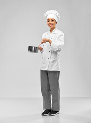 culinary and people concept - happy smiling female chef in toque and jacket with saucepan cooking food over grey background