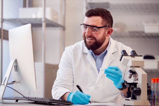 Male Lab Worker Wearing White Coat Recording Test Results On Computer