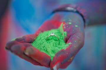 Hand holding engagement ring in green powder 