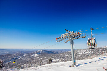 Obraz premium Cabin lift for sheregesh kemerovo ski resort on background of mountains and blue sky, sunny day