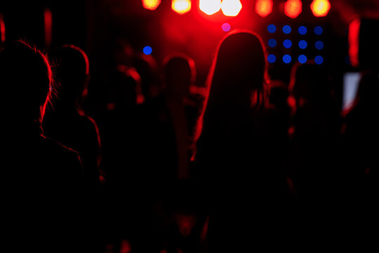 cheering crowd in front of bright red stage lights. Silhouette image of people dance in disco night club or concert at a music festival.