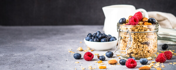 Granola with fresh berries in the glass jar. Healthy dessert or snack at stone table. Long format.