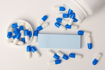 Closeup of a blank blue sticky note and blue-white pills spilling out of pill bottle. Medical concept. Blank space for future important events announcements