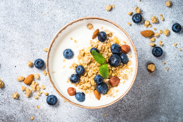 Yogurt with granola and blueberries at stone table in craft plate. Top view with copy space.