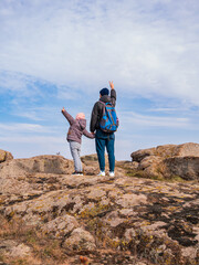 Travelers father daughter with raised hands walking climbing on mountain summit enjoying aerial view blue cloudy sky back view together. Active Lifestyle Family Travel Scenic landscape hiking Backpack