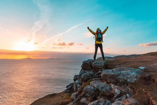 Happy successful man with arms up on the top of cliff in Scotland at sunset