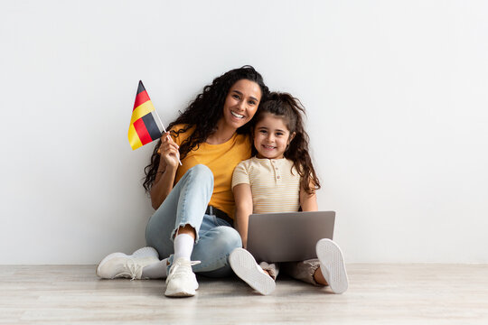 Happy Arab Mom And Little Daughter Holding Laptop And Flag Of Germany