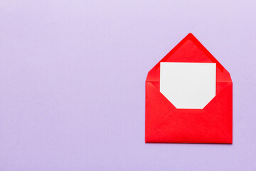 Red paper envelope with empty white card and heart on colored background. top view valentines day...