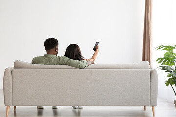 Back view of hugging black lovers watching TV at home - Powered by Adobe