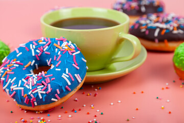 Multicolored donuts and a cup of coffee on a pink background.