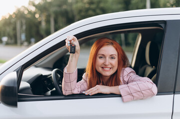 Woman bought first car. Joyful female sitting in new car and shows keys.