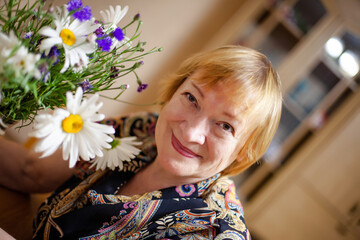 Naklejka premium Old woman with wildflowers at home