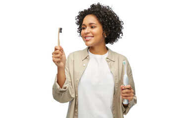 eco living, zero waste and sustainability concept - portrait of happy smiling young woman comparing wooden and electric toothbrushes over white background