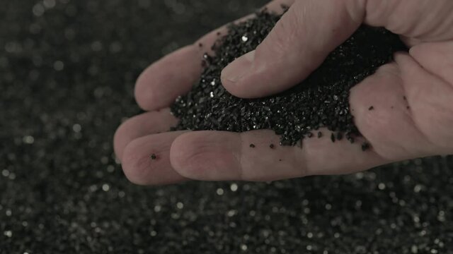 bare caucasian hand holding and pouring black activated carbon coconut charcoal powder of small fraction in slow motion