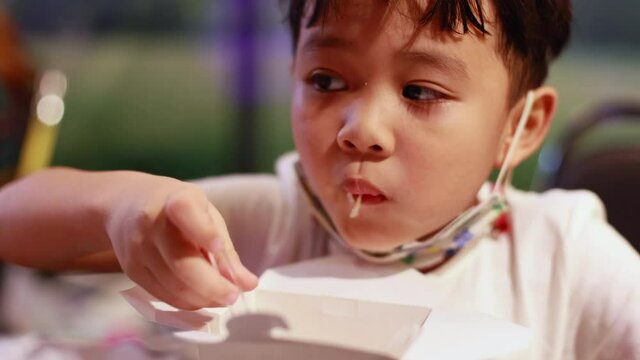 cute asian boy eating delicious food from lunch box