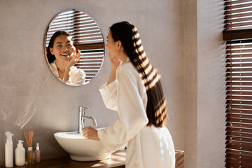 Back view of happy asian woman applying face care product