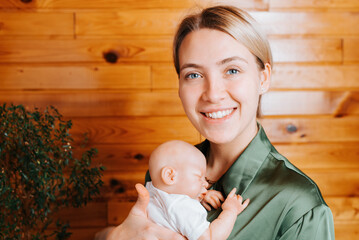 Portrait of smiling young woman holding realistic newborn baby reborn doll in arms and looking at...