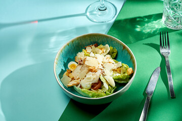 Caesar salad with chicken, croutons and parmesan. Bright backgrounds. Hard shadows, selective focus.