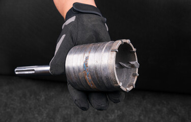 Closeup of hole saw cutter on hand in work glove on black background. Construction worker holding...