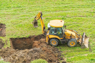 Obraz premium Tractor excavator digs a hole for installing a collector line and pipes.