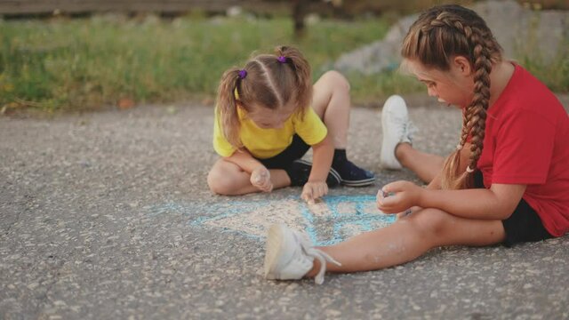 children draws a picture house with chalk on the road. happy family kid dream concept. children play with crayon. happy childhood concept. kid drawing art the house. happy family two sisters playing