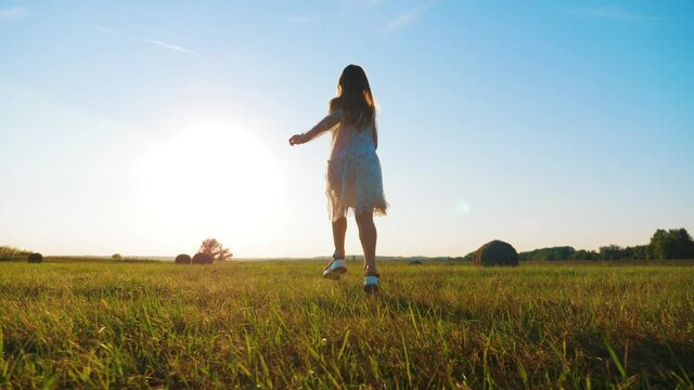 Happy childhood. Cheerful girl are running in the green meadow. Back view of girl running on flower meadow at evening twilight. Teen girl running on meadow with sunset. Happy family concept.