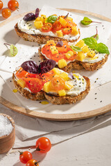 Italian bruschettas with roasted tomatoes, cream cheese, pineapple slices and herbs on a kitchen countertop. Prepared to serve
