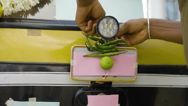 Close up of hands tying chilli and lemon to auto rickshaw front - concept of religious, spritual believes and superstition.